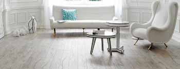 Ein modernes Wohnzimmer mit einem weißen Sofa, einem stilvollen Sessel und einem Couchtisch auf einem hellen Laminatboden, minimalistisch dekoriert.