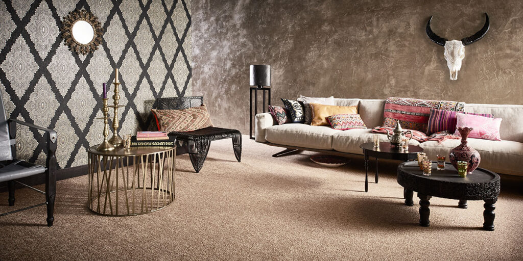 Ein stilvolles Wohnzimmer mit einem Dekor im Bohème-Stil mit Teppichboden, verschiedenen Kissen in bunten Möbelstoffen und einer kreativen Wandgestaltung mit gemusterter Tapete und Unitapete.