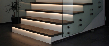 Eine Treppe mit Glasgeländer, LED-Leuchten und Produkten.