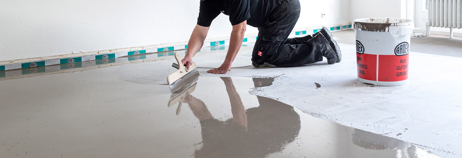 Ein Mann arbeitet auf einem Betonboden in einem Raum, umgeben von seinen Referenzen. Raumausstattung Merget | Goethestraße 43 | 63814 Mainaschaff