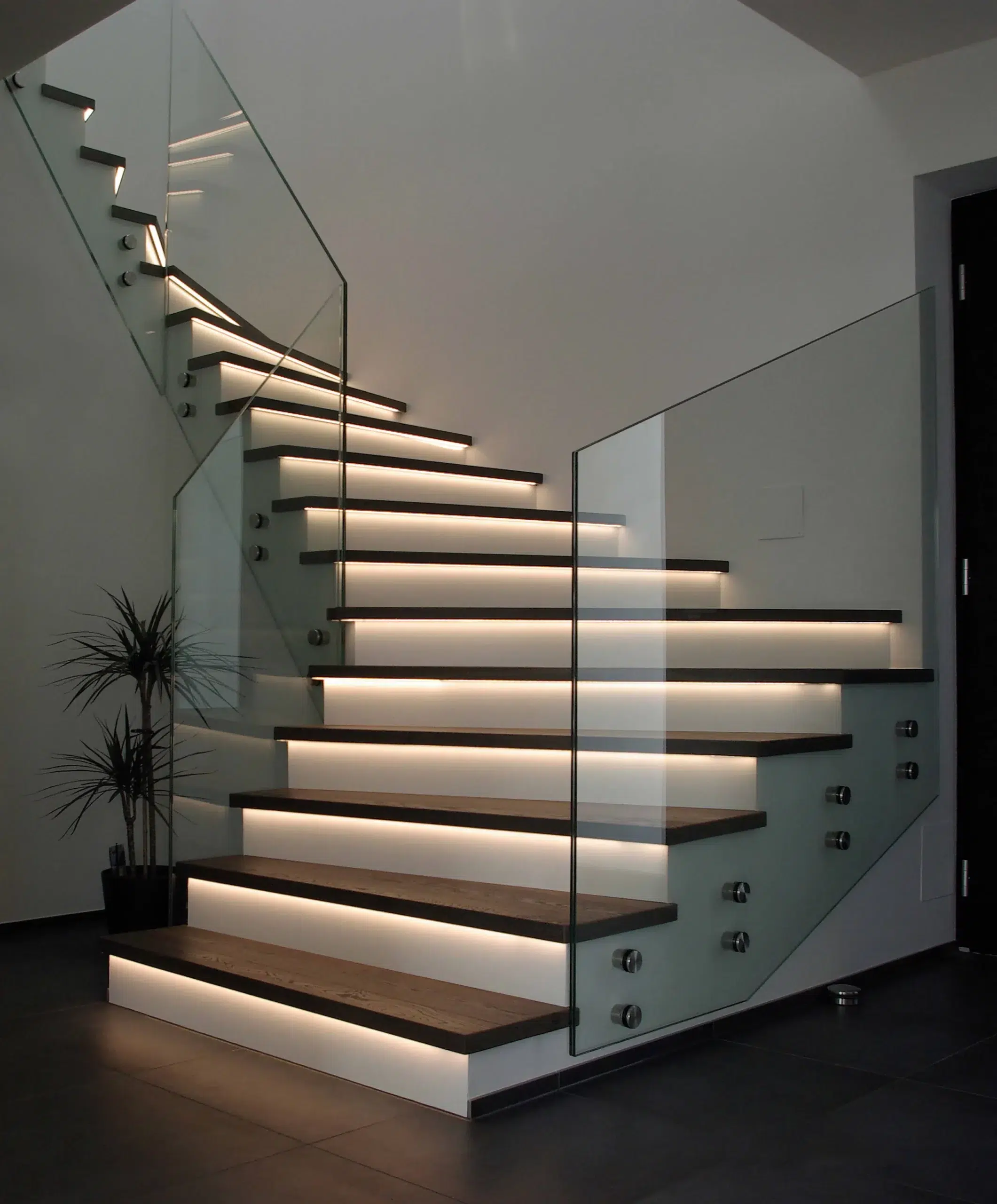 Eine moderne Treppe mit Treppenstufen aus Holz, einem Glasgeländer und Beleuchtung.