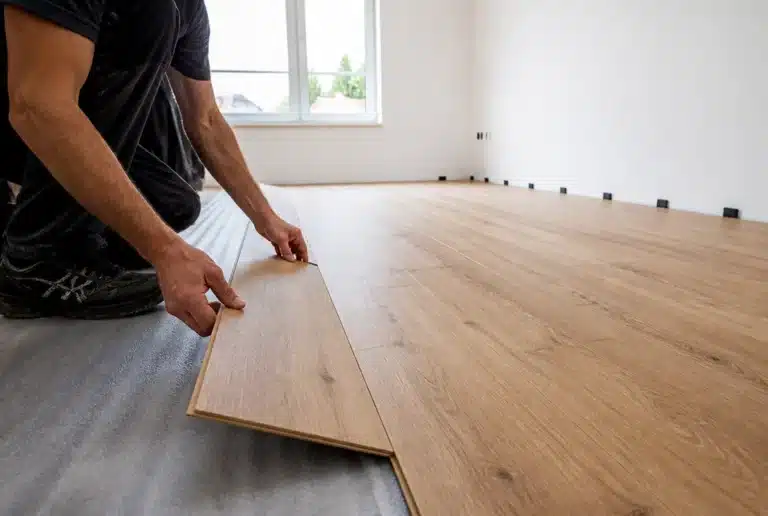 Laminat verlegen: Klick-Diele wird auf Dämmunterlage eingesetzt, Distanzkeile an der Wand