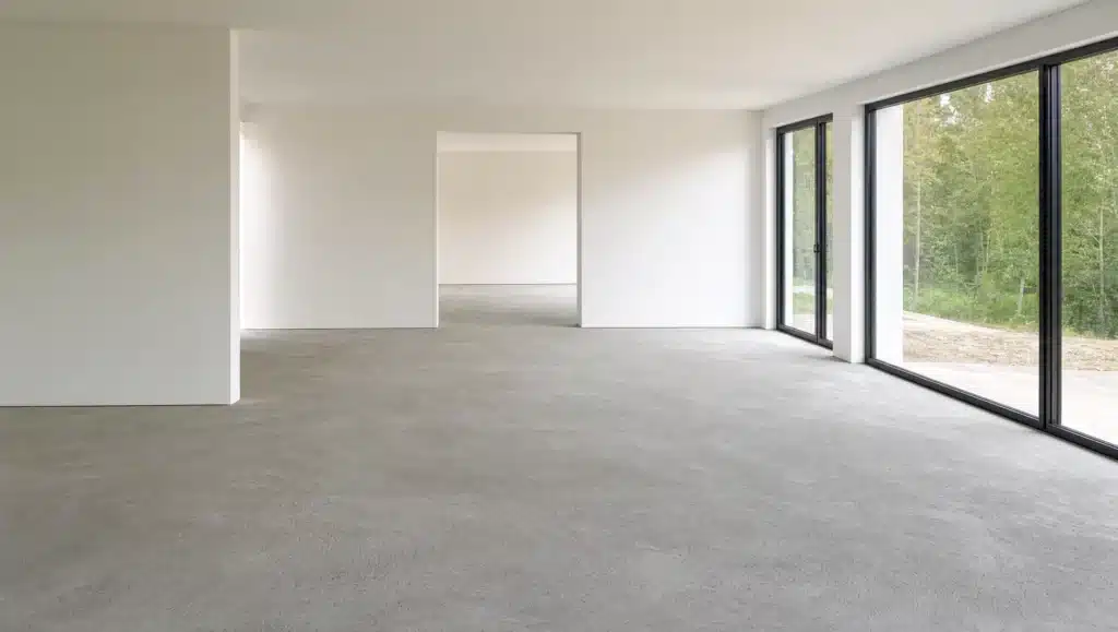 Roher, gespachtelter Estrich in einem hellen, unmoeblierten Neubau-Wohnzimmer - der vorbereitete Untergrund vor der Verlegung